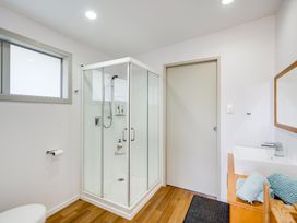 A bathroom with a glass shower enclosure a toilet a sink with folded towels and a mirror above at Mahanga Dunes Retreat - Mahia Holiday Home in Mahia Peninsula
