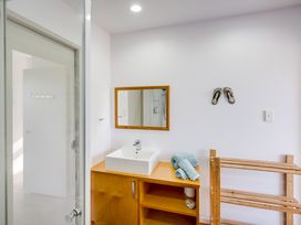 A bathroom with a wooden cabinet, a white sink, a mirror, towels on the counter, a wooden rack, and a pair of sandals on the wall at Mahanga Dunes Retreat - Mahia Holiday Home in Mahia Peninsula