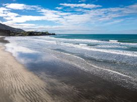 A beach with waves and a hill in the distance under a partly cloudy sky at Mahanga Dunes Retreat - Mahia Holiday Home in Mahia Peninsula