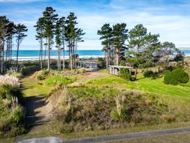 A grassy area with tall trees two small buildings and ocean in the background at Mahanga Dunes Retreat - Mahia Holiday Home in Mahia Peninsula
