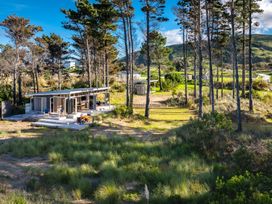 A small house with an open patio surrounded by trees and grassy dunes at Mahanga Dunes Retreat Mahia Holiday Home Mahia Peninsula