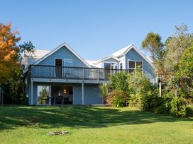 A two story blue house with a balcony and lawn surrounded by trees at Okere Jetty Escape  Rotoiti Holiday Home