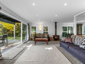 A living room with sofas a coffee table a wood stove and large sliding glass doors opening to a deck at Okere Jetty Escape  Rotoiti Holiday Home in Okere Falls