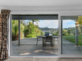 A sliding glass door opening to a wooden deck with a table and chairs overlooking trees and water at Okere Jetty Escape in Okere Falls