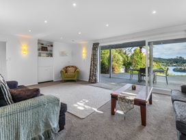 A living room with sofas coffee table and armchair next to sliding glass doors opening to a deck with outdoor furniture at Okere Jetty Escape -  Rotoiti Holiday Home in Okere Falls