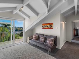 A room with a sofa and pillows next to a sliding glass door leading to a balcony with trees visible outside at Okere Jetty Escape  Rotoiti Holiday Home in Okere Falls