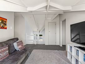 A loft room with a gray sofa, a white cubed media unit with a TV, and a carpet at Okere Jetty Escape  Rotoiti Holiday Home in Okere Falls