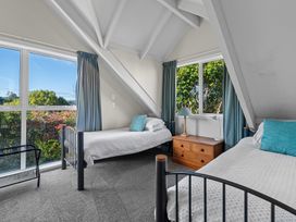 A bedroom with two single beds a wooden nightstand and large windows at Okere Jetty Escape  Rotoiti Holiday Home in Okere Falls