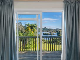A sliding glass door opening to a wooden deck with a view of trees water and hills beyond at Okere Jetty Escape -  Rotoiti Holiday Home in Okere Falls