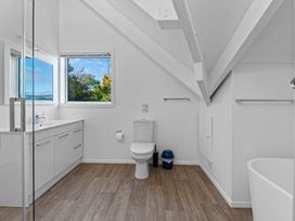 A bathroom with a toilet, vanity with sink, bathtub, and window showing trees at Okere Jetty Escape in Okere Falls