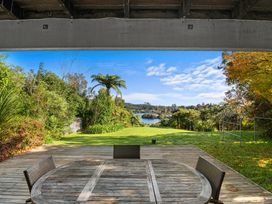 A wooden outdoor table with chairs on a deck overlooking a grassy yard and a lake at Okere Jetty Escape Rotoiti Holiday Home in Okere Falls