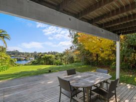 An outdoor covered wooden deck with a table and four chairs overlooking a grassy yard and a lake at Okere Jetty Escape in Okere Falls