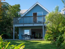 A two-story house with a balcony and outdoor seating surrounded by trees and plants at Okere Jetty Escape  Rotoiti Holiday Home in Okere Falls