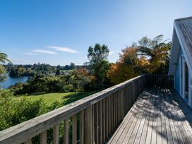 A wooden balcony overlooking a grassy area with trees and a lake in the background at Okere Jetty Escape  Rotoiti Holiday Home in Okere Falls