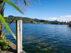 A wooden post with the number 54A by a lake with hills and houses in the background at Okere Jetty Escape  Rotoiti Holiday Home in Okere Falls
