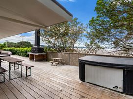 An outdoor wooden deck with benches table a barbecue hot tub and trees at Heron's Hideaway Snells Beach