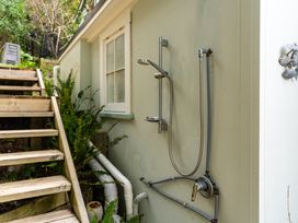 An outdoor shower attached to the exterior wall of a building next to wooden stairs and plants at Heron's Hideaway - Snells Beach