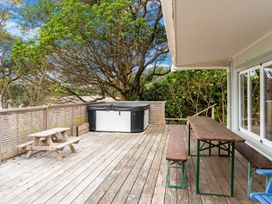 A wooden deck with a hot tub a small wooden picnic table and a wooden table with benches at Heron's Hideaway - Snells Beach Holiday Home in Snells Beach
