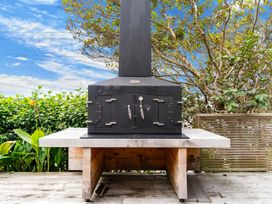 An outdoor wood-fired oven on a wooden deck with plants and trees in the background at Heron's Hideaway - Snells Beach Holiday Home in Snells Beach