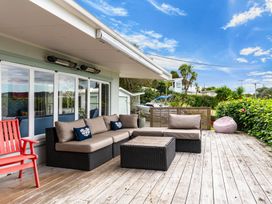 An outdoor deck with a sectional sofa a red wooden chair a square coffee table and a bean bag at Heron's Hideaway - Snells Beach Holiday Home in Snells Beach
