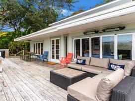 An outdoor deck with a beige sectional sofa two armchairs a wooden table and benches at Heron's Hideaway - Snells Beach Holiday Home in Snells Beach