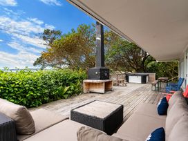 An outdoor deck with a wooden floor a black fireplace beige couches a wicker table colorful chairs a picnic table and greenery at Heron's Hideaway - Snells Beach Holiday Home in Snells Beach