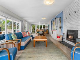 A living room with blue sofas wooden table fireplace and dining area in the background at Heron's Hideaway - Snells Beach Holiday Home in Snells Beach