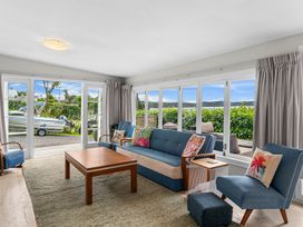 A living room with blue chairs a sofa a wooden coffee table and large windows showing an outdoor view at Heron's Hideaway - Snells Beach Holiday Home in Snells Beach