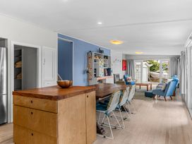 A living room and dining area with wooden table chairs blue armchairs and island bench at Heron's Hideaway - Snells Beach Holiday Home in Snells Beach