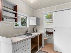A laundry room with a double sink countertop open shelves with toilet paper and an adjacent small bathroom at Heron's Hideaway in Snells Beach