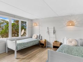 A bedroom with two single beds bedside tables and large windows showing trees at Heron's Hideaway - Snells Beach Holiday Home in Snells Beach