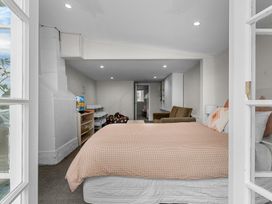 A bedroom with a bed a brown armchair a bean bag a television and shelves at Heron's Hideaway - Snells Beach Holiday Home in Snells Beach