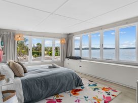 A bedroom with a bed and large windows overlooking water at Heron's Hideaway - Snells Beach