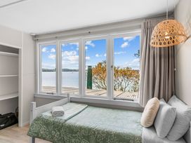 A bedroom with a bed and large windows overlooking the water at Heron's Hideaway - Snells Beach