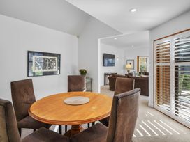 A dining area with a round wooden table and four brown chairs next to a living room with brown sofas and a wall-mounted television at Stylish Fendalton Townhouse - Prime Location in Christchurch