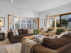 A living room with brown sofas two floral armchairs a chessboard on a glass coffee table with a view outside at Stylish Fendalton Townhouse in Christchurch