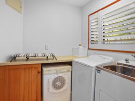 A laundry room with a dryer, washing machine, stainless steel sink, ironing board, and window with shutters at Stylish Fendalton Townhouse Prime Location Christchurch
