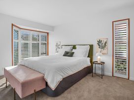 A bedroom with a large bed green headboard and white bedding pink bench at foot of bed nightstand with lamp two botanical prints and windows with shutters at Stylish Fendalton Townhouse - Prime Location Christchurch
