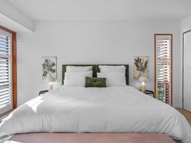 A bedroom with a large bed with white bedding green pillows and botanical prints on the wall at Stylish Fendalton Townhouse - Prime Location in Christchurch