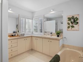A bathroom with beige cabinets a sink a large mirror plantation shutters on the window a bathtub with a towel and a plant on the countertop at Stylish Fendalton Townhouse - Prime Location Christchurch