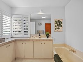 A bathroom with a bathtub sink vanity cabinets plant and framed leaf artwork at Stylish Fendalton Townhouse - Prime Location Christchurch