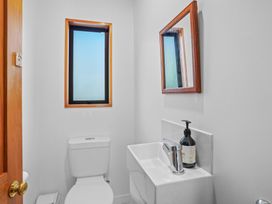 A small bathroom with a toilet, a sink with a faucet and soap dispenser, a mirror, and a window framed in wood at Stylish Fendalton Townhouse - Prime Location Christchurch