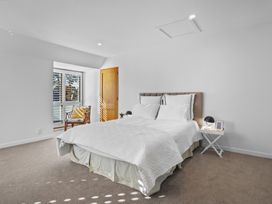A bedroom with a bed with white bedding a wooden chair near a window and a small bedside table with a lamp and photo at Stylish Fendalton Townhouse - Prime Location in Christchurch