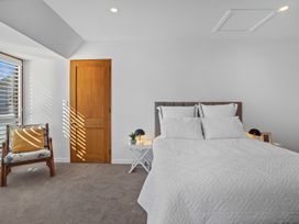 A bedroom with a bed with white bedding a wooden chair with cushions a wooden door and bedside tables with lamps at Stylish Fendalton Townhouse - Prime Location in Christchurch