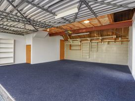 An empty garage with a blue carpet floor shelves on the left wall wooden door and storage racks on the back wall at Stylish Fendalton Townhouse - Prime Location in Christchurch