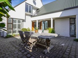 An outdoor patio area with a wooden dining table and chairs surrounded by white brick walls and plants at Stylish Fendalton Townhouse Prime Location Christchurch