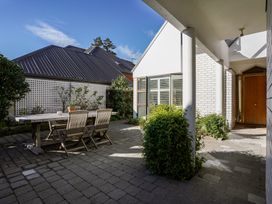 A paved outdoor patio with a wooden table and chairs near a white brick house with plants and wooden door at Stylish Fendalton Townhouse - Prime Location Christchurch