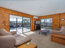 A living room with a television and sliding glass door at Seabreeze Surf House - Whitianga