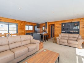 A living room with sofas and a kitchen counter at Seabreeze Surf House - Whitianga