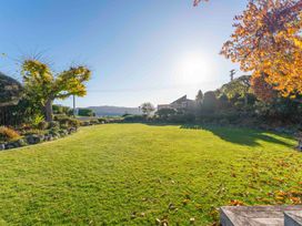 A garden with a green lawn trees and bushes under a clear sky at Waterside Bliss - Taupo Holiday Home in Taupo Central